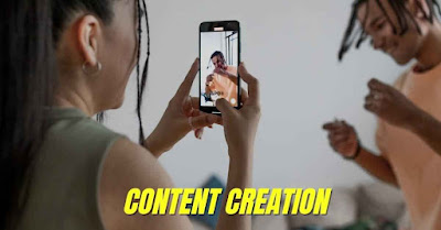 A woman is filming a man with her smartphone, with the words "CONTENT CREATION" overlaid on the image. It represents the niche content creation business idea for women.